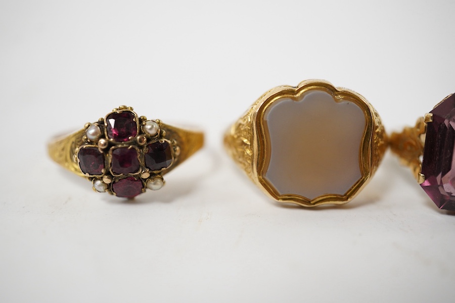 A group of four rings, comprising: a chalcedony signet ring with engraved floral shoulders, size L, partial British hallmarks for 15ct gold; a synthetic ruby and diamond five-stone ring, size N, stamped 18CT; a ring set